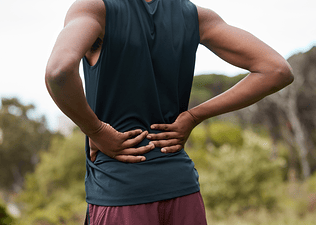 A close-up photo of a runner with their hands on their lower back, experiencing pain.