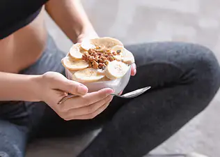 An athlete eating a yogurt bowl with bananas and oats after a workout. Learn whether you should eat protein before or after a workout in this article.