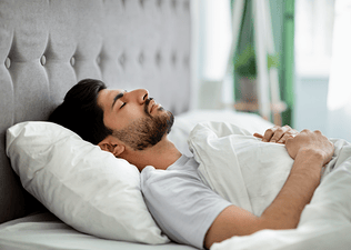 A man lying down on his back in bed practicing a body scan meditation.
