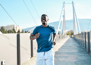 A smiling man running across a bridge on a sunny day.