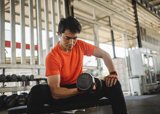 A man doing a dumbbell concentration curl with a dumbbell in the gym.