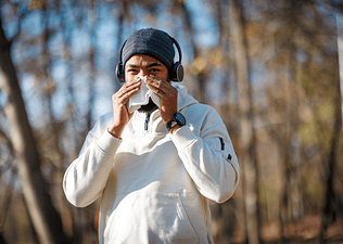 A man going on a run on a chilly day while stopping to blow his nose. He is running while sick.