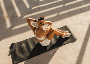 A woman doing a core workout while sitting on a yoga mat outside.
