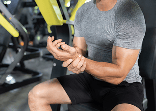 Close-up photo of a man holding his left wrist in the gym. He is dealing with wrist pain from weight lifting.