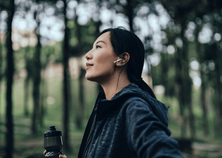 A confident athlete standing in the forrest, holding a water bottle, and looking resilient. Learn how to build resilience in this article.