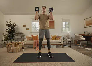Man holds dumbbells while doing hamstring exercises during a Peloton strength workout at home