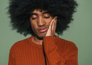 In this image for an article about feeling sleepy after eating, a man is closing his eyes and putting a hand on his cheek in tiredness.