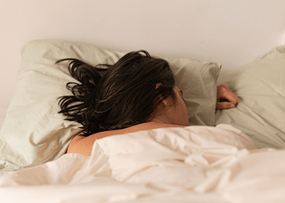 A woman sleeping in bed on her belly. Learn whether or not it is bad to sleep with wet hair in this article.