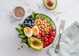 A wholesome bowl filled with macronutrient sources, including avocado, hard-boiled egg, chickpeas, spinach, tomato, blueberries, and cucumbers.