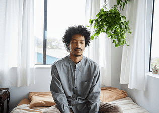 A man meditating at home in a sunny room as part of his habit loop.