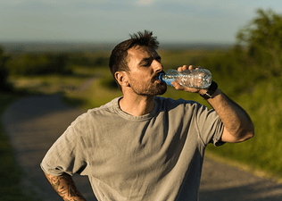 A man drinking water during a workout. He's outside on a sunny day.