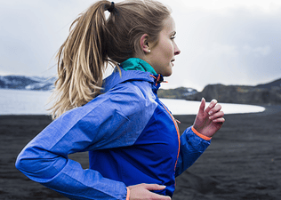 A side-view photo of a woman running outside on a chilly day.