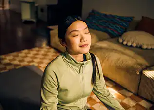 A woman practicing breathwork on a yoga mat in her living room.