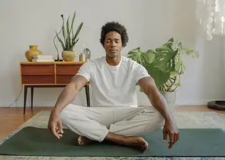 A man meditating with his eyes closed. He's sitting criss-cross on a yoga mat with his arms resting on his knees.