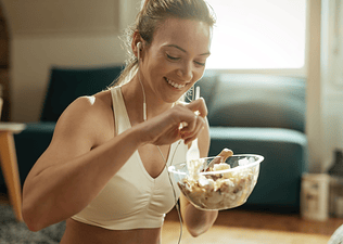 A smiling woman eating a salad after a workout.