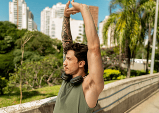 A man working out outside on a sunny day, stretching his arms up overhead.