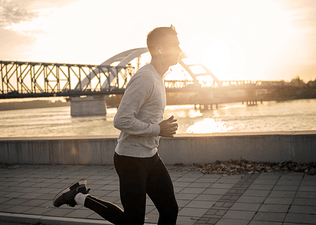 Side view of a man jogging outside near a river in the morning sunlight.