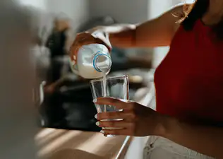 Close-up photo of a woman pouring a glass of milk in her kitchen. She's drinking milk to help build muscle. 