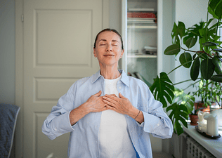 A woman meditating at home with her hands on her chest.