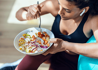 A woman eating dinner (a veggie-packed grain bowl) before or after a workout. She's in workout clothes and is leaning against a big exercise ball. 