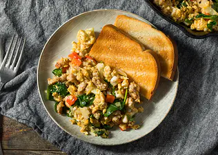 A healthy breakfast option of scrambled eggs with veggies mixed in and some whole-wheat toast on the side.