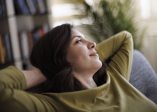 A woman relaxing at home, meditating with her eyes open in a soft gaze.