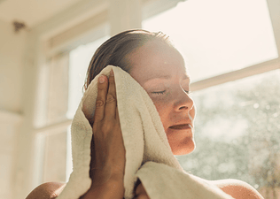 A woman drying her face with a towel as she's sweating after a shower.