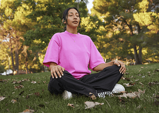 A young woman sitting outside in the grass doing a meditation for anxiety.
