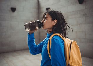 A woman having creatine while sipping from a black shaker bottle after an outdoor workout. 