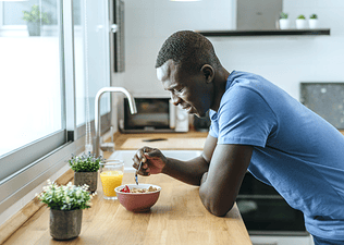 A happy man leaning on his kitchen counter while eating breakfast before a workout.
