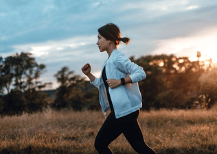 A woman working to improve her cardiovascular endurance by going on a jog in the park at dusk.