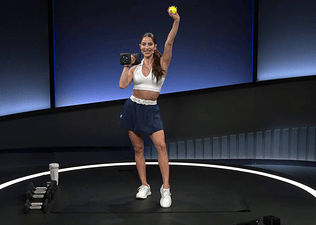 Peloton instructor Assal Arian poses with a dumbbell and tennis ball during a Peloton strength for tennis class.