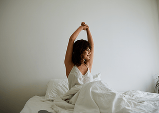 A woman stretching her arms above her head in bed after waking up.