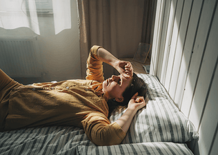 An overtired woman looking stressed out while lying in her bed in the early morning.