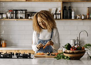 A woman smiling and peeling a carrot in her kitchen to eat more vegetables.