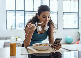 A woman eating after a workout and looking at her phone.