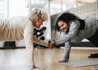 Two people engaging in friendly competition, exercising together and giving each other a high-five while in a plank position on exercise mats.