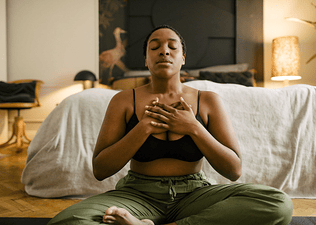 A woman practicing gratitude meditation at home. She's sitting down with her hands on her chest.
