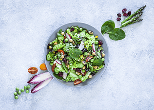 A flat-lay photo of a green salad on a neutral countertop. The salad includes high-protein vegetables including green peas and spinach.
