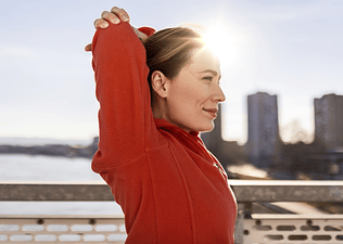 A woman happily breathing with her arms resting above her head after she finishes a morning outdoor workout.