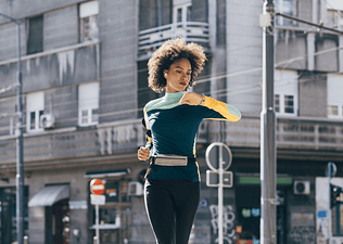 A runner checking her heart rate on a watch monitor while going for a run outside.