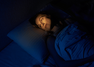 A woman lying awake in bed, experiencing racing thoughts at night.