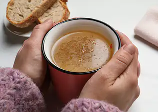 Close-up photo of a pair of hands holding a cup of bone broth.