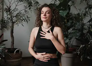 A woman practicing belly breathing. She is sitting tall with one hand on her chest and one hand on her belly, her eyes closed.
