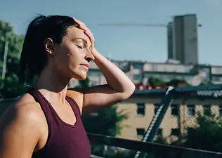 A woman exercising in the heat. She's sweating with her hand on her forehead while walking outdoors.