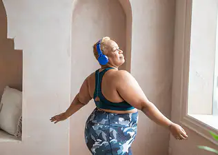 A woman dancing while wearing exercise clothes and headphones.