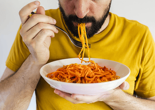 A close-up photo of a man eating a bowl of spaghetti as he eats before a marathon.