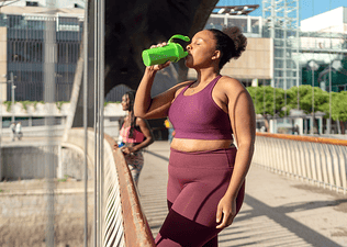 A woman drinking a smoothie after an outdoor cardio workout.