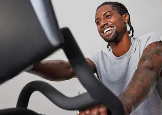 Exerciser on Peloton Bike, tapping screen, and smiling