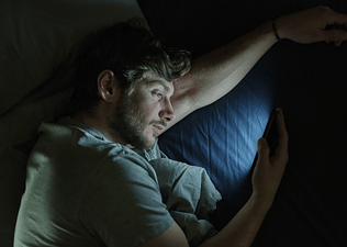 A man lying in bed and staring at his phone at night.